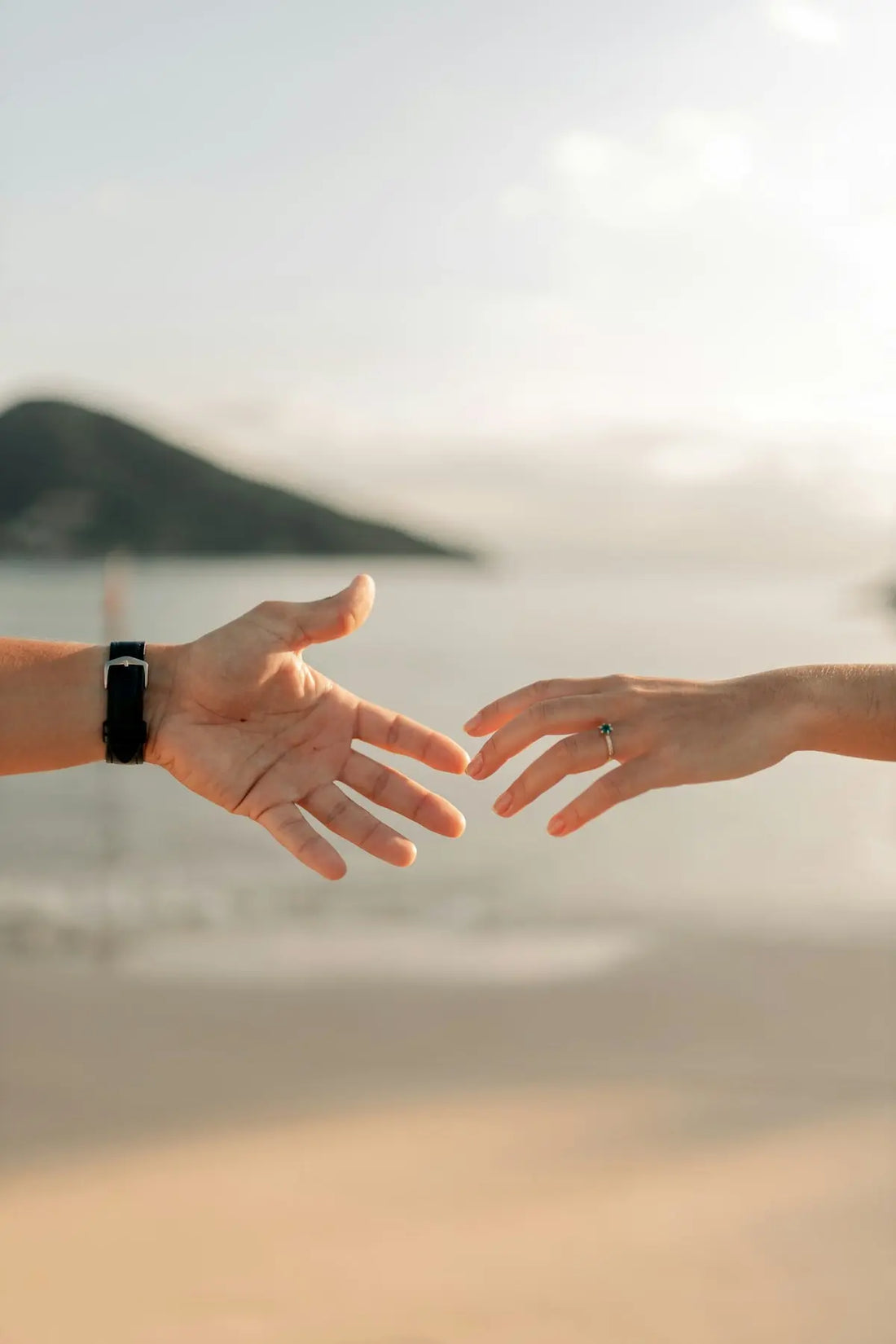 Two hands reaching out towards each other on a beach