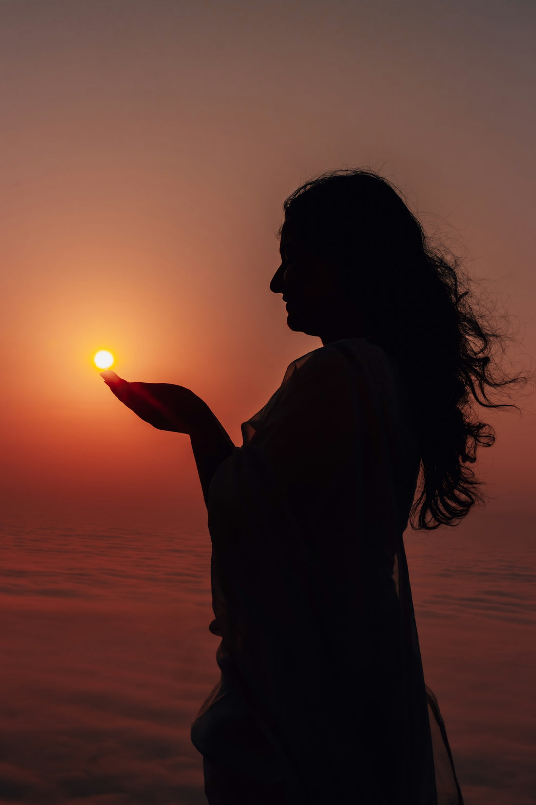 Woman holds the sun in her hands at sunset