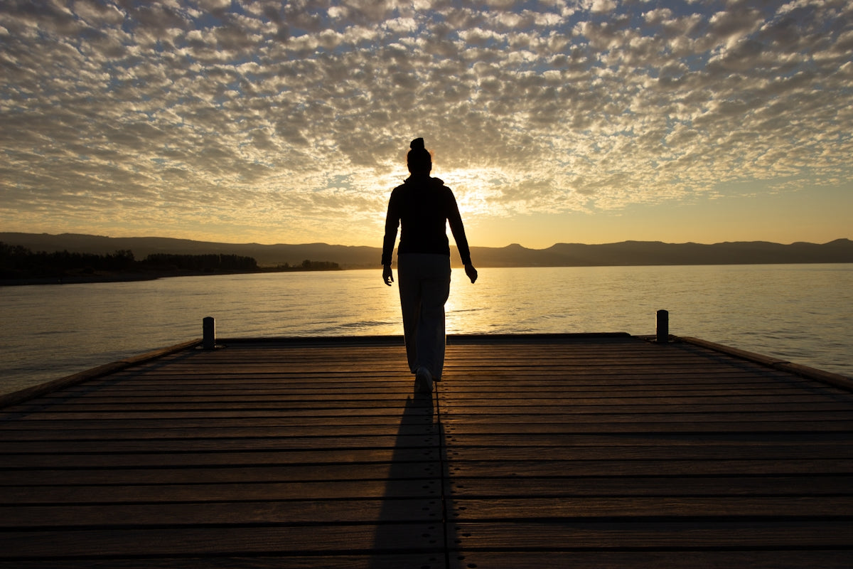A person walks on a pier at sunset.