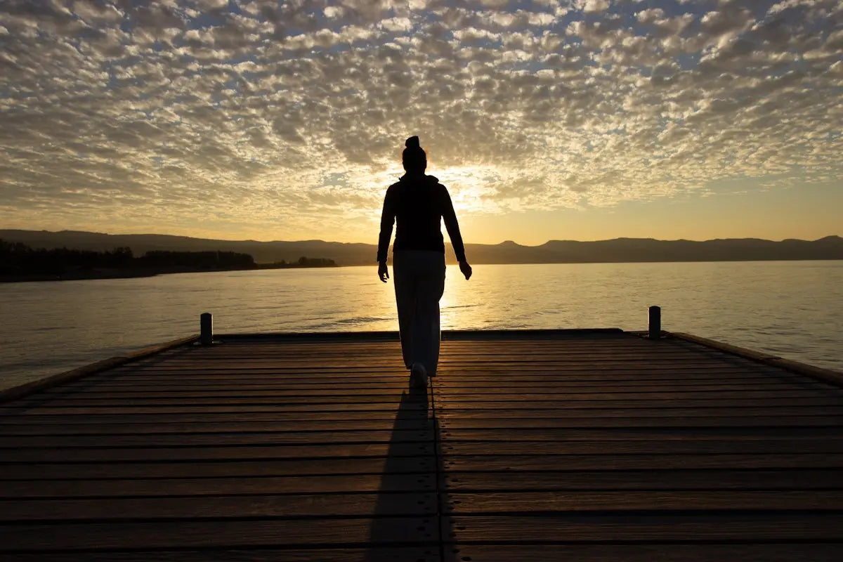 A person walks on a pier at sunset.