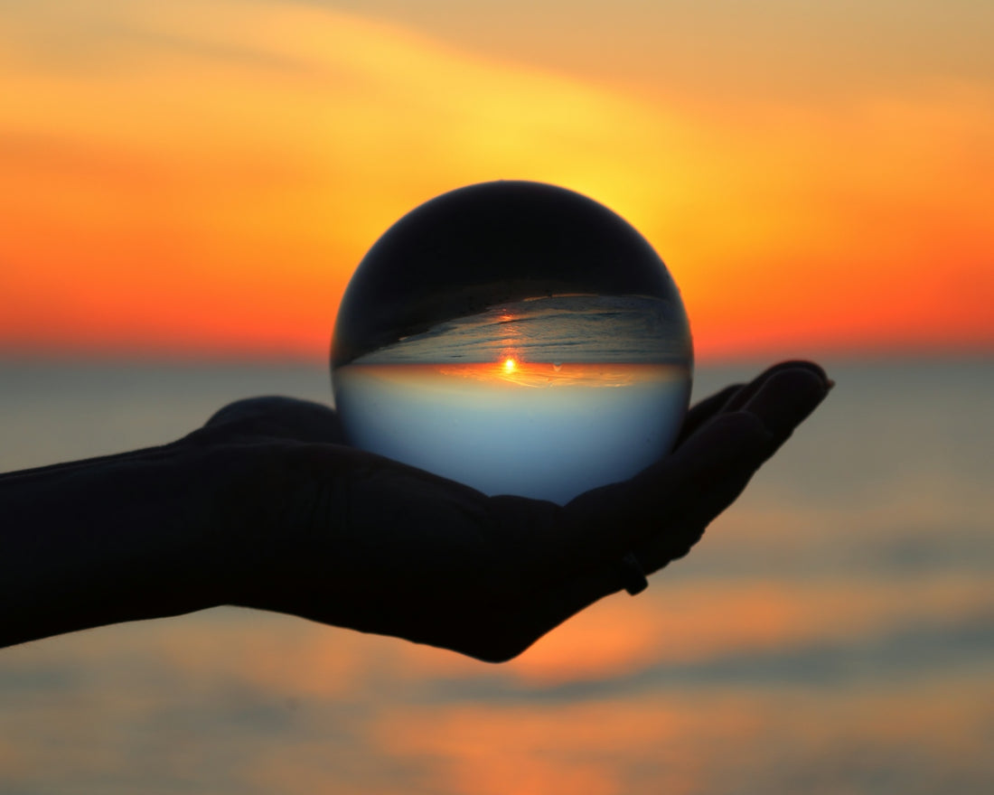 Silhouette hand holding crystal ball reflecting inverted sunset